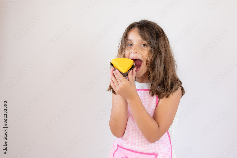 Pretty little girl with a apron on and eating a piece of cake Pretty little girl with a apron on and eating a piece of cake