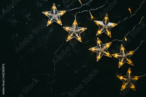 Garland stars yellow light on black stone background. Christmas beautiful background. Top view, flat lay, copy space.