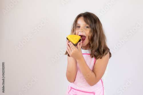 Pretty little girl with a apron on and eating a piece of cake
