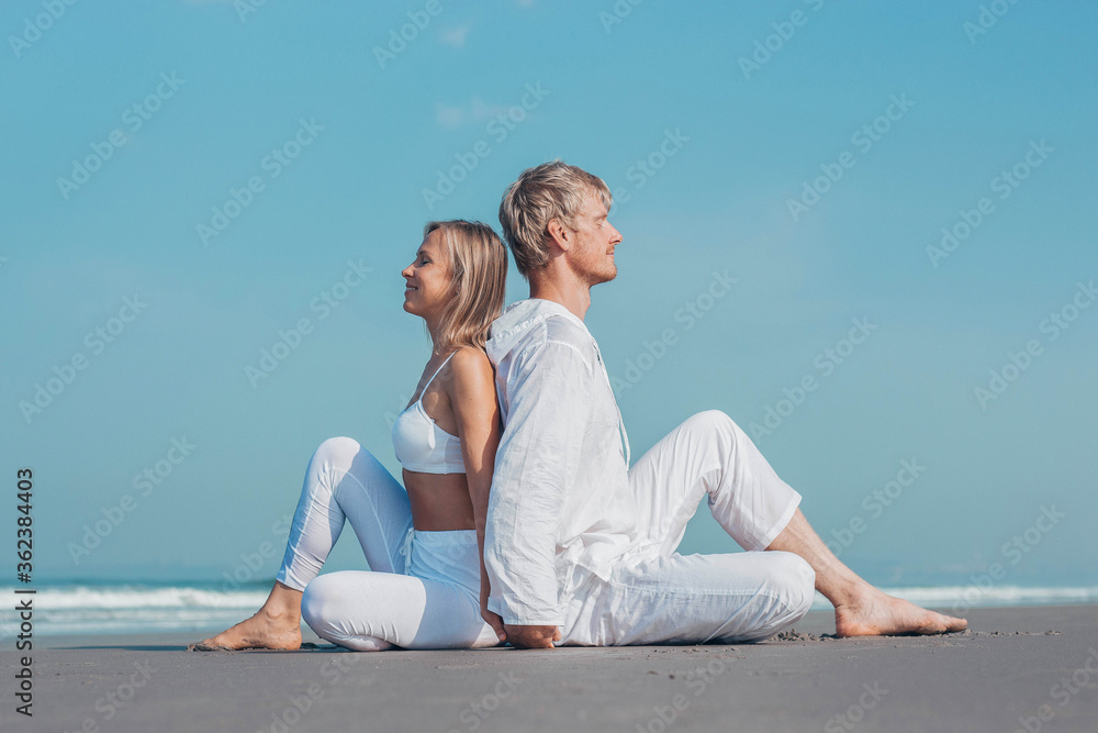 guy and girl in white clothes are sitting on the ocean and holding hands namaste
