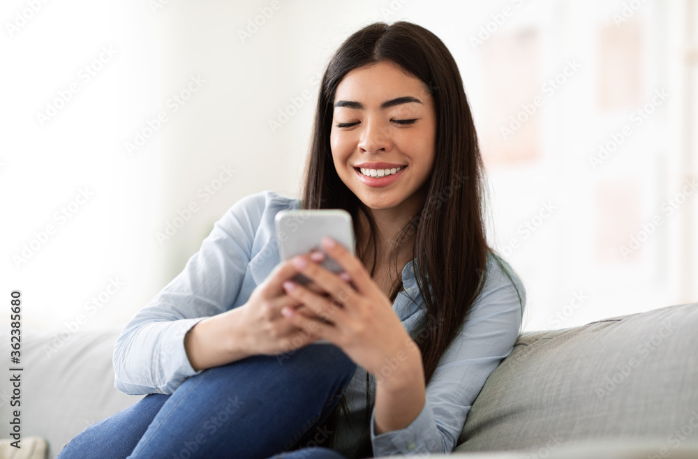 Smiling Asian Girl Using Smartphone At Home, Checking Social Media Smiling Asian Girl Using Smartphone At Home, Checking Social Media