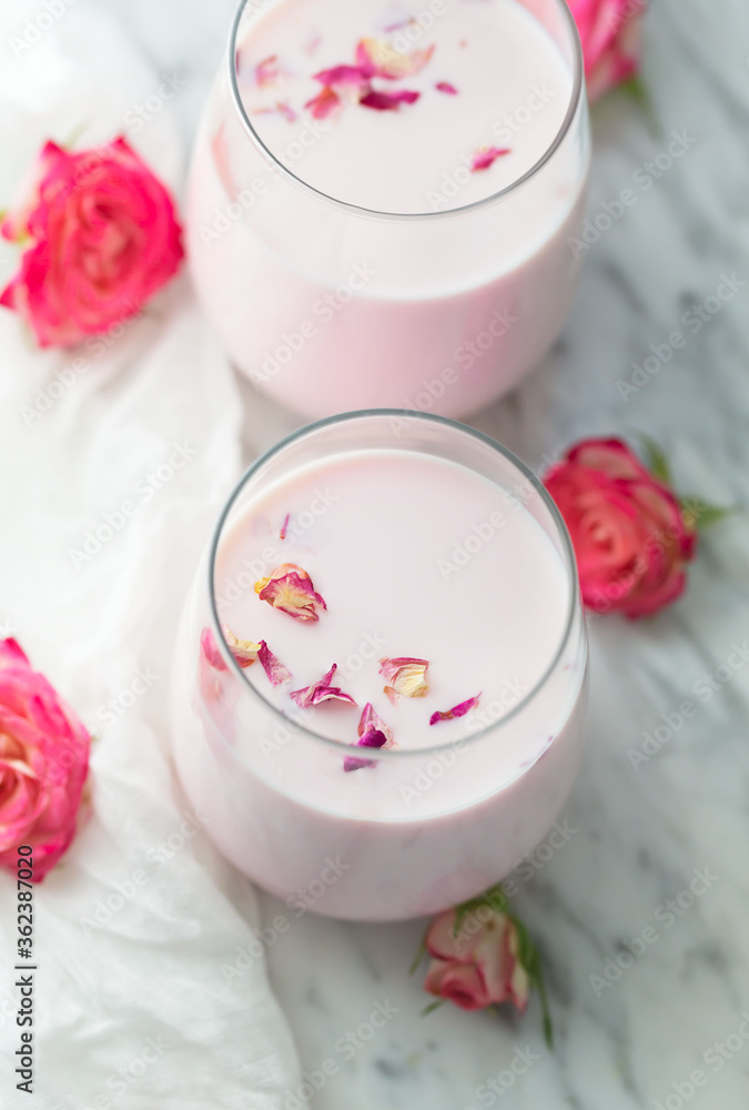 Moon milk prepares with pink rose flower. Trendy relaxing bedtime drink form Ayurvedic traditions. Top view, close up