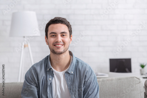 Young man in casual sits on sofa in living room interior and makes video recordings