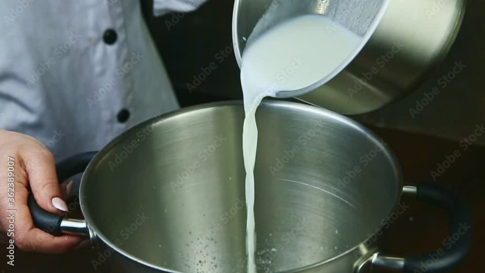 slow motion closeup woman pours hot milk from small saucepan into metal bowl slow motion closeup woman pours hot milk from small saucepan into metal bowl