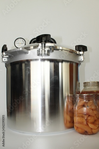 Pressure canner and  jars of preserved food on a white background in vertical format