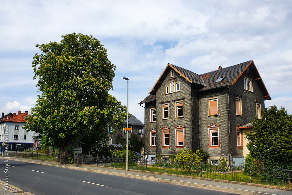 Altes schiefernes Haus mit braunen Rolladen steht an der Hauptstraße umgeben von grünen Bäumen und Büschen. Bayern, Deutschland. Altes schiefernes Haus mit braunen Rolladen steht an der Hauptstraße umgeben von grünen Bäumen und Büschen. Bayern, Deutschland.