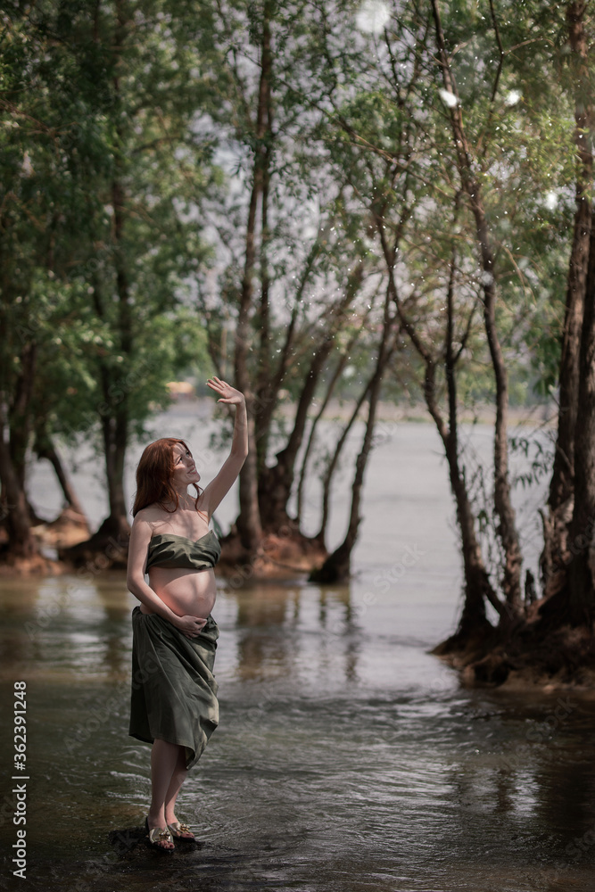 Fototapeta premium red-haired pregnant girl in the forest closes her hand from the sun