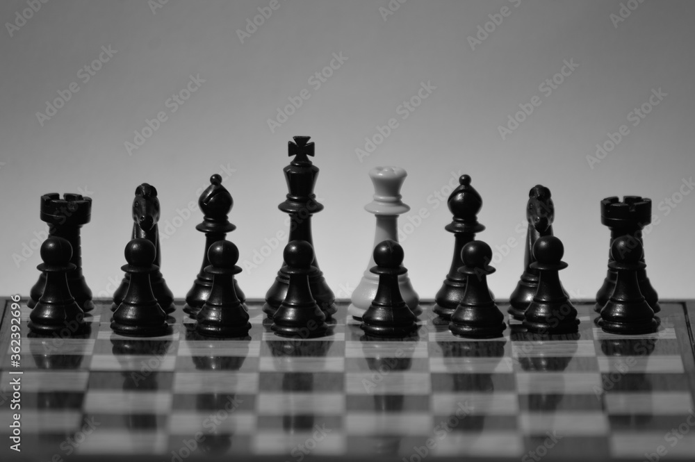 Black and white shot of a white queen surrounded by black chess pieces on chessboard