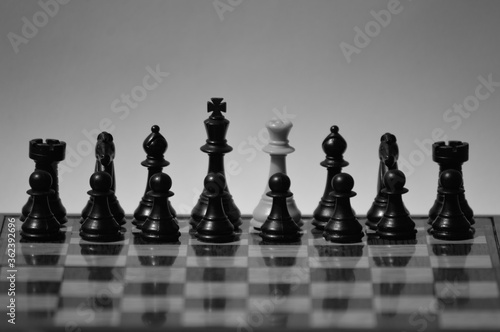 Black and white shot of a white queen surrounded by black chess pieces on chessboard