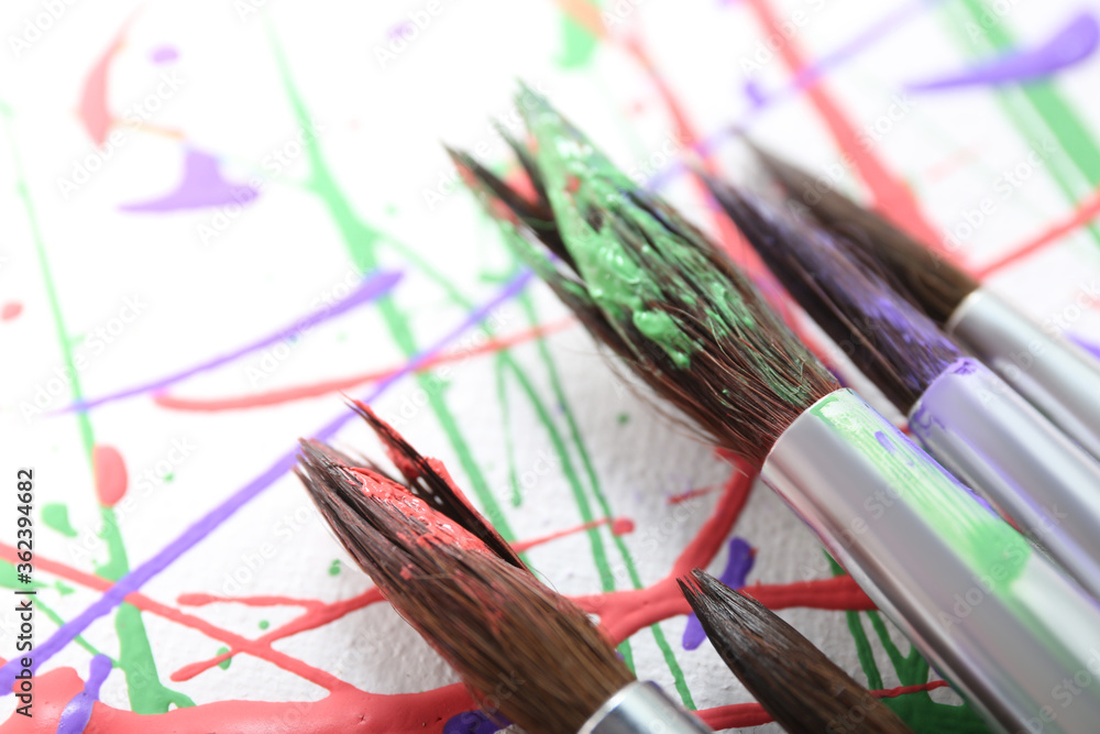 Obraz premium Brushes on canvas with colorful paint splashes, closeup. Art and creativity
