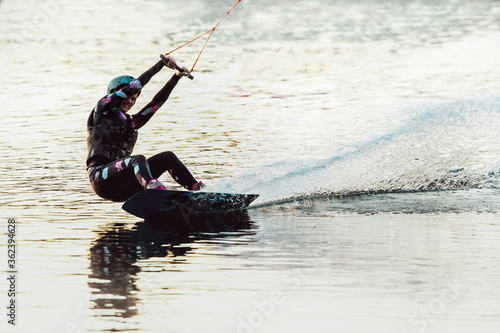Wake Board a women does a trick at sunset on the Board on the water splashes