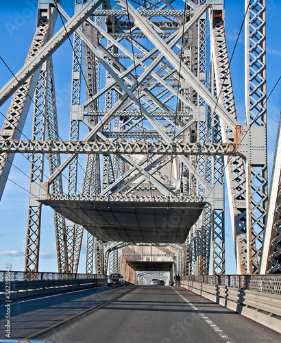This vertical traffic image is a steel truss bridge from inside the bridge perspective. Road has light traffic traveling on it in the daytime with bright blue skies. © Valerie Garner