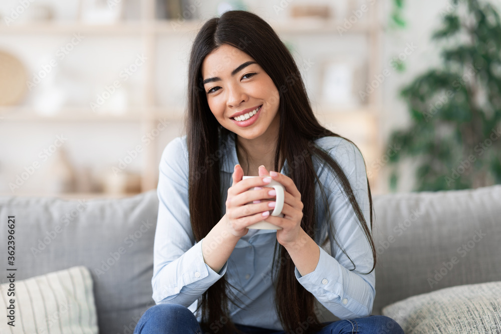 Beautiful asian girl relaxing on sofa at home with cup of coffee Beautiful asian girl relaxing on sofa at home with cup of coffee