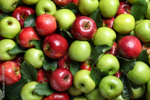 Pile of tasty ripe apples with leaves as background, top view