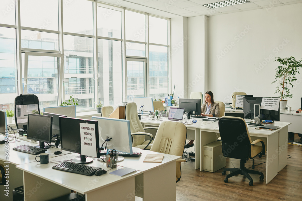 Young elegant businesswoman sitting by desk in the corner of modern office Young elegant businesswoman sitting by desk in the corner of modern office