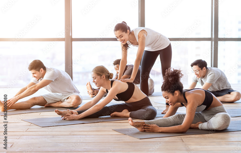 Obraz premium Yoga instructor assisting young woman in doing stretching exercises during group lesson