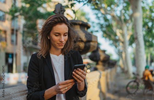 Obraz na płótnie focus on businesswoman in suit calling on cell phone in park, portrait elegant woman with smartphone and wireless earphones on sun day in street city, female manager using mobile phone outdoors w salonie