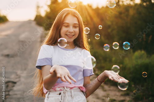 Cute girl with a beautiful smile catches soap bubbles on the background of a beautiful sunset.