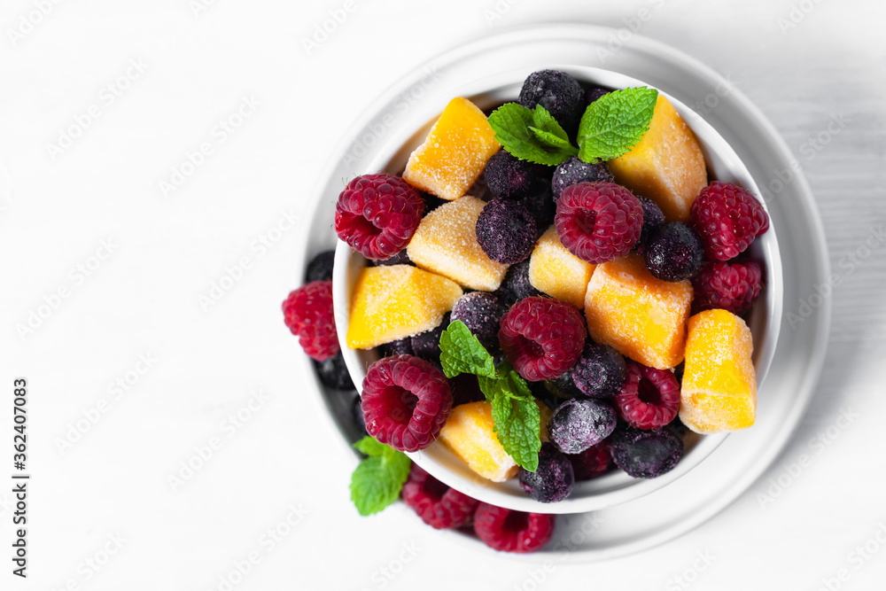 Frozen fruits: mango, raspberry, blueberry with fresh green mint, white bowl. Concept of healthy eating, low calories dessert, summer refreshing meal. Light background copy space. Flat lay top view Frozen fruits: mango, raspberry, blueberry with fresh green mint, white bowl. Concept of healthy eating, low calories dessert, summer refreshing meal. Light background copy space. Flat lay top view