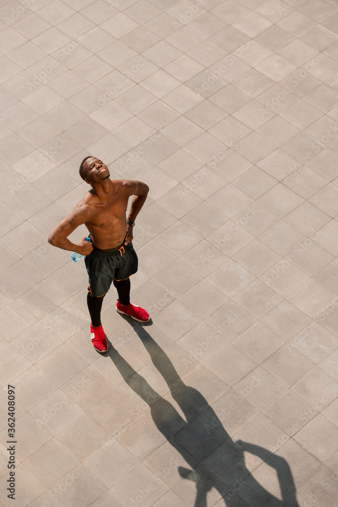 Young tired shirtless man of African ethnicity standing in urban environment
