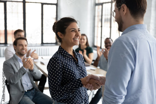 Bilde på lerret Happy proud excited Indian ethnicity employee get promotion receive praises from boss and cheering and congratulations from diverse staff members shake hands with chief