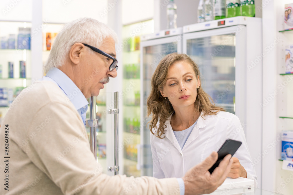 Senior man with smartphone showing name of new medicine to young consultant Senior man with smartphone showing name of new medicine to young consultant