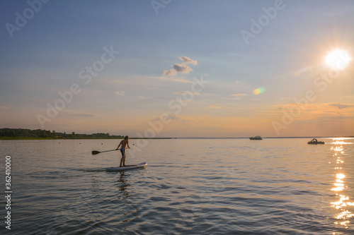 Young boy on the lake is rowing on the inflatable sup towards the sunset © TOMASZ