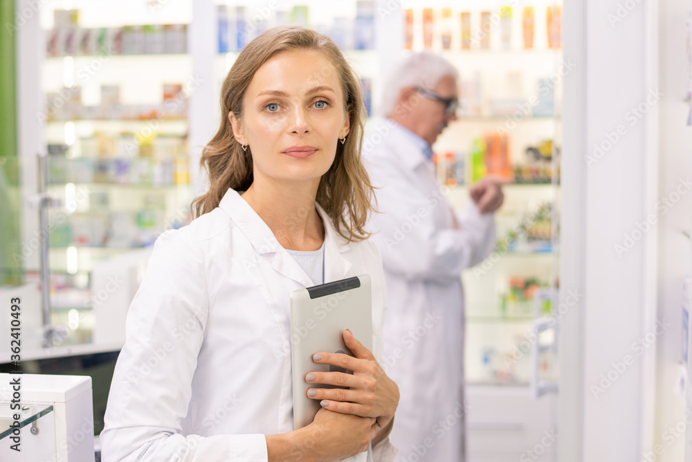 Pretty young pharmacist or worker of contemporary drugstore with digital tablet