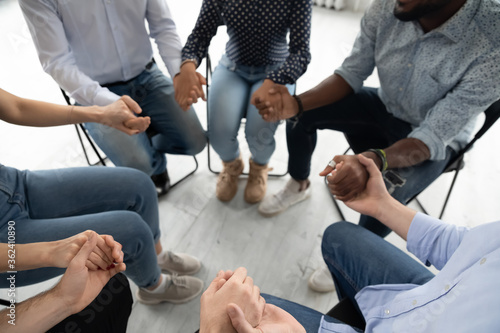 People sit in circle hold hands involved at group therapy session. Religious girls guys pray together for salvation. Psychological support, corporate training for spirit, unity strengthening concept