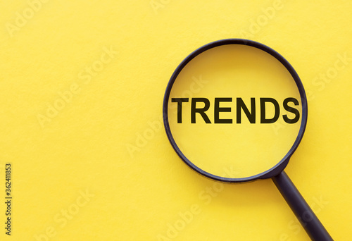 TRENDS text written on magnifier glasses, on yellow background. Main trend of changing something. Popular and relevant topics. New trends in business. Recent and latest trend. Evaluation methods. photo