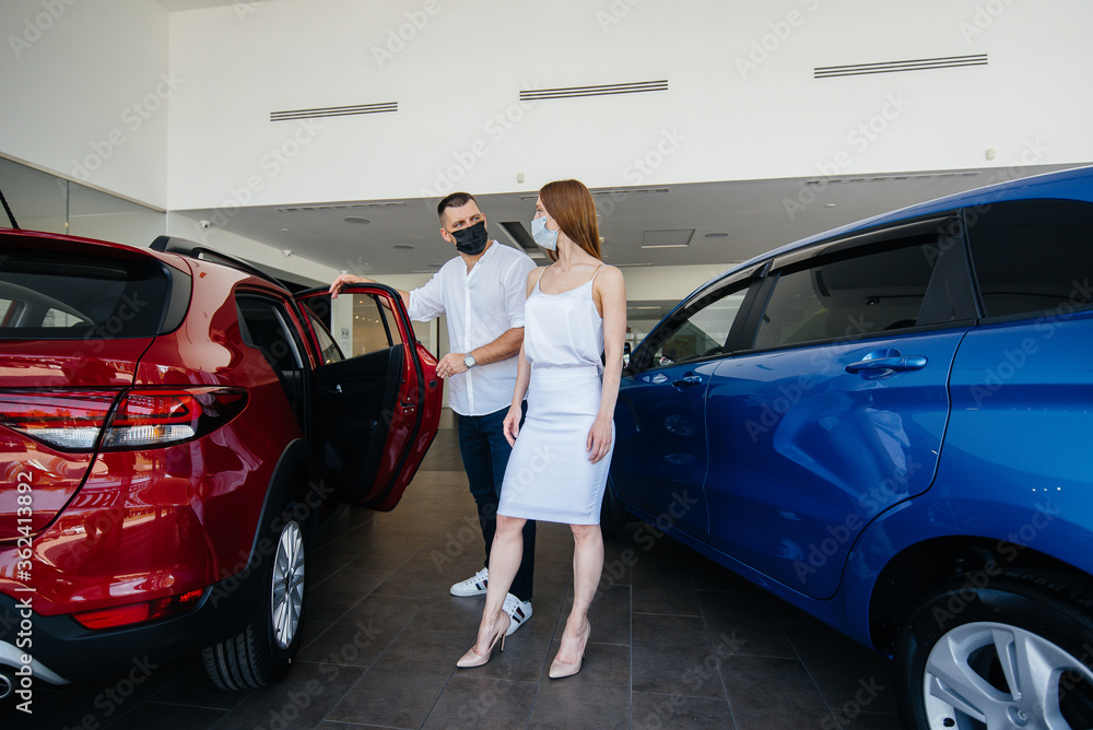Young couple in masks selects a new vehicle and consult with a representative of the dealership in the period of the pandemic. Car sales, and life during the pandemic