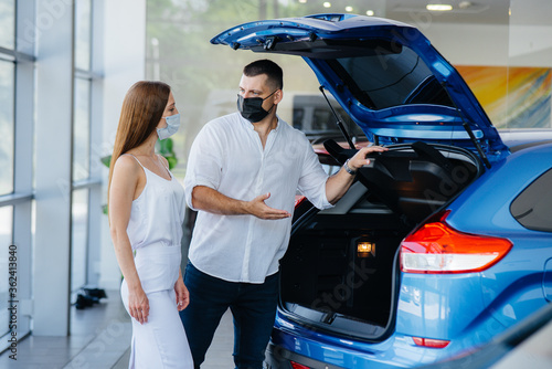 Young couple in masks selects a new vehicle and consult with a representative of the dealership in the period of the pandemic. Car sales, and life during the pandemic