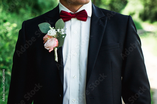 groom with a boutonniere, in a suit and a red bow-tie