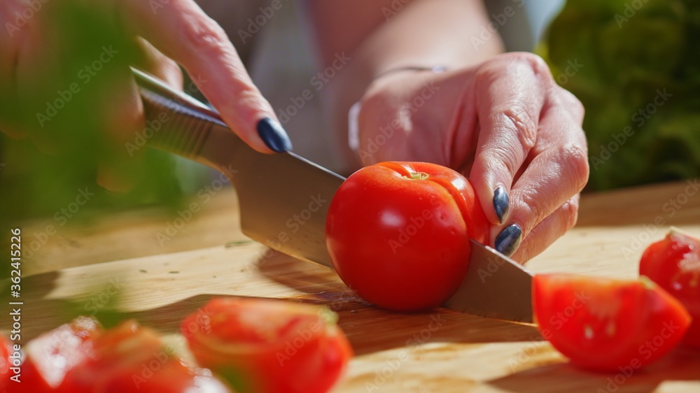 Woman slicing tomato and vegetables for cooking on kitchen table. Closeup hands. Cosy dark room. Woman slicing tomato and vegetables for cooking on kitchen table. Closeup hands. Cosy dark room.