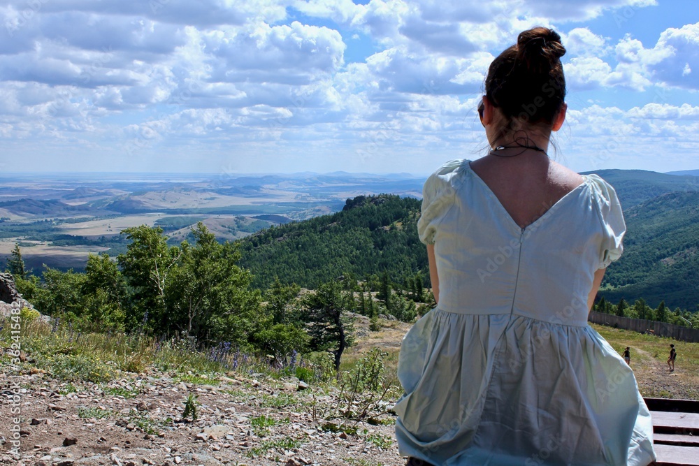 A young girl on top of a mountain enjoys a panoramic view of the mountains from above. Summer perfect landscape