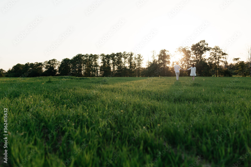 Happy young couple walking on the field with green grass on the sunset. Love story