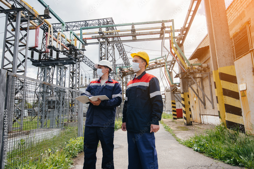 Engineers electrical substations conduct a survey of modern high-voltage equipment in the mask at the time of pandemia in the evening. Energy. Industry Engineers electrical substations conduct a survey of modern high-voltage equipment in the mask at the time of pandemia in the evening. Energy. Industry