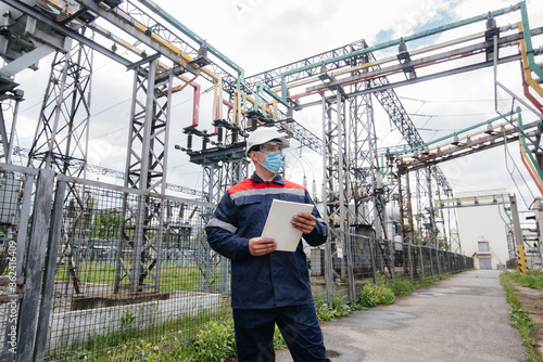 An electrical substation engineer inspects modern high-voltage equipment in a mask at the time of pondemia. Energy. Industry © Andrii