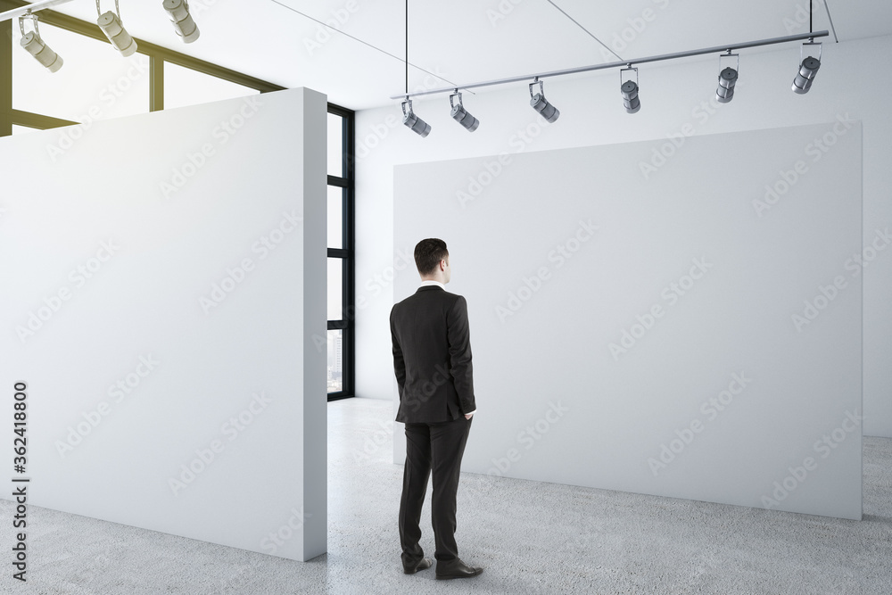 Businessman standing in clean gallery interior and looking on blank wall. Businessman standing in clean gallery interior and looking on blank wall.