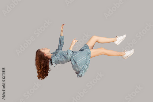 Floating in air. Relaxed girl in vintage ruffle dress levitating keeping eyes closed, sleeping while flying mid-air, having comfortable peaceful dream. full length studio shot isolated on gray, indoor photo