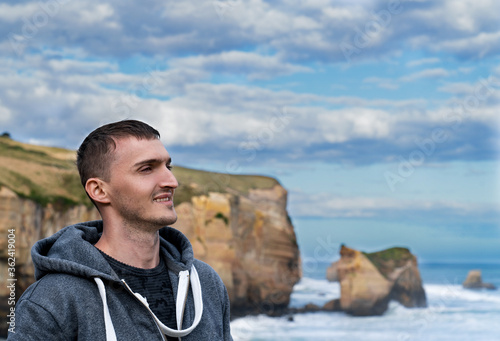 The smiling face of a young man on a background of sky, mountains and sea
