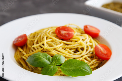 Close-up plate with italian pasta with pesto sauce, garnished with cherry tomatoes and basil leaves