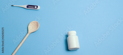 Concept protective equipment against pandemic, coronavirus, top view. Wooden spoon, pills and capsule bottle, thermometer on blue background, isolated. Free, blank space for text. Banner for web site © Maksim