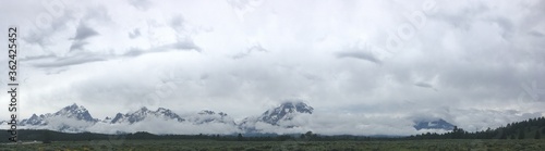 Panorama of majestic Grand Teton Mountains mystically peaking out through the clouds