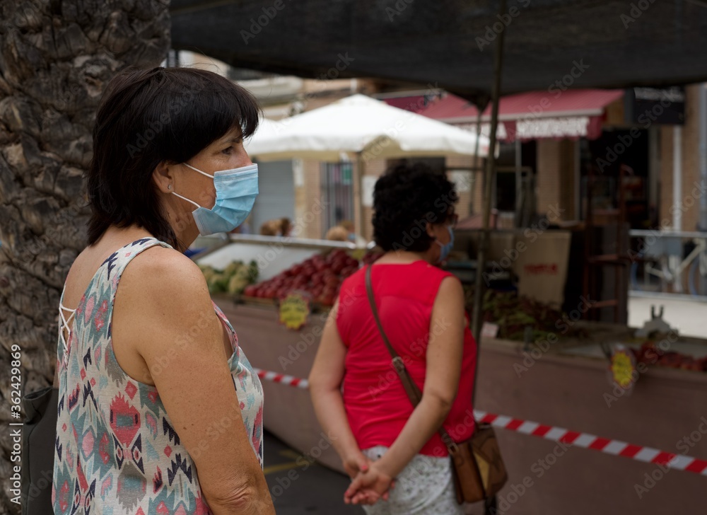 Middle aged woman wearing surgical face mask queuing up for shopping in a street market. Global COVID-19 pandemic concept image. Social distance. New normal lifestyle