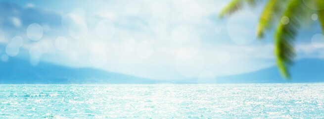 Blurred summer natural marine tropical blue background with palm leaves and sunbeams of light. Sea and sky with white clouds. Panoramic banner with copy space