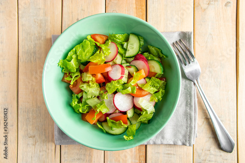 Recipe for vegetable salad with tomatoes, cucumbers and radishes. Seasonal dish on wooden background. Vegan food for diet.