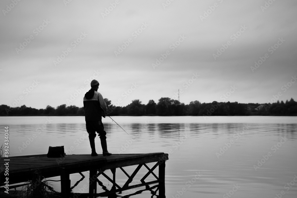 Silhouette of a fisherman standing on the pier, black and white photo