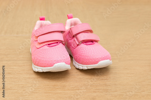 Child's pink summer sneakers are against a green wall The shoes are close up.