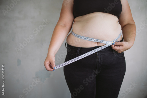 Overweight woman measuring waist with measure tape, close up image. Weight loss, motivation, fat burning photo